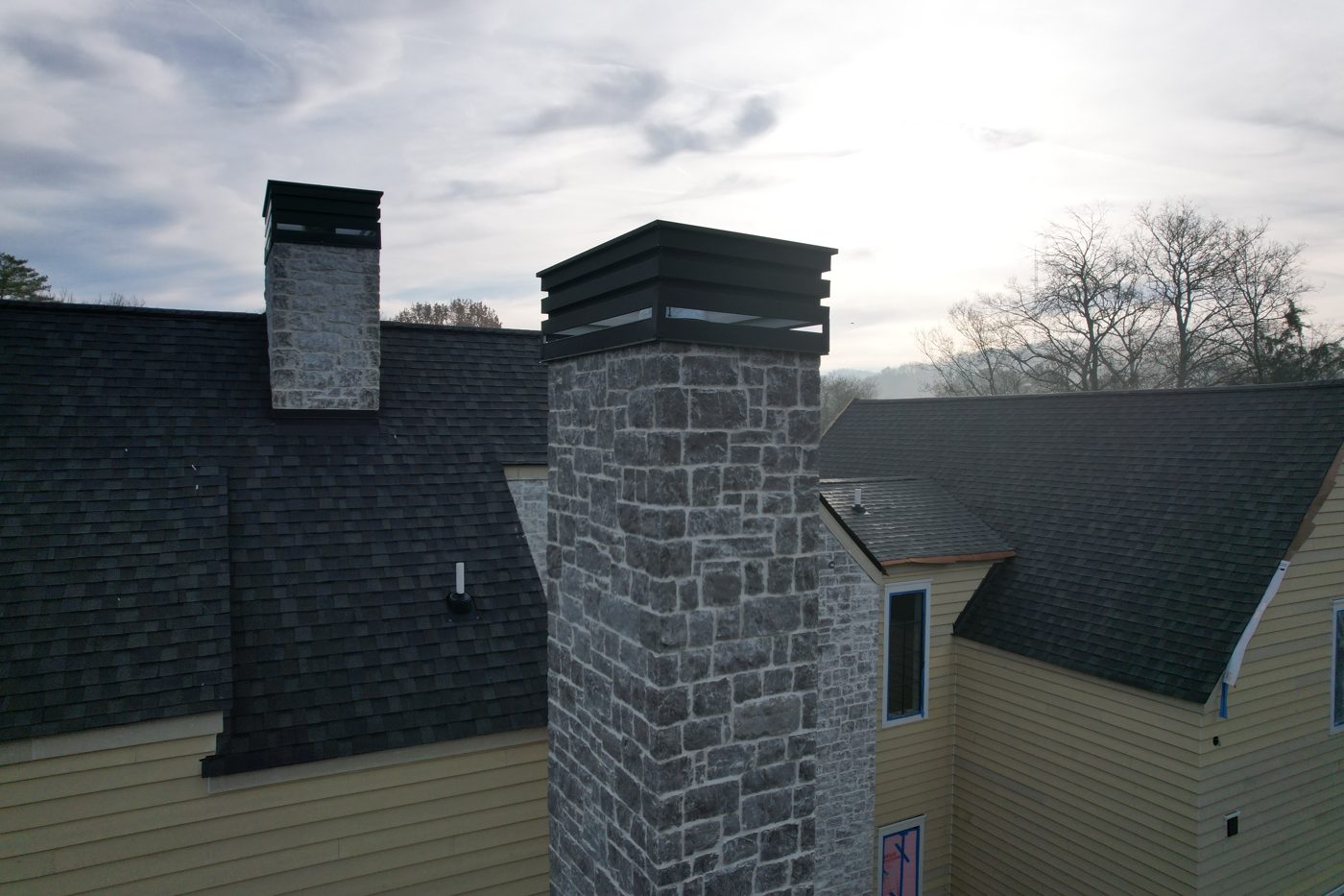 Custom black metal chimney caps on stone chimneys