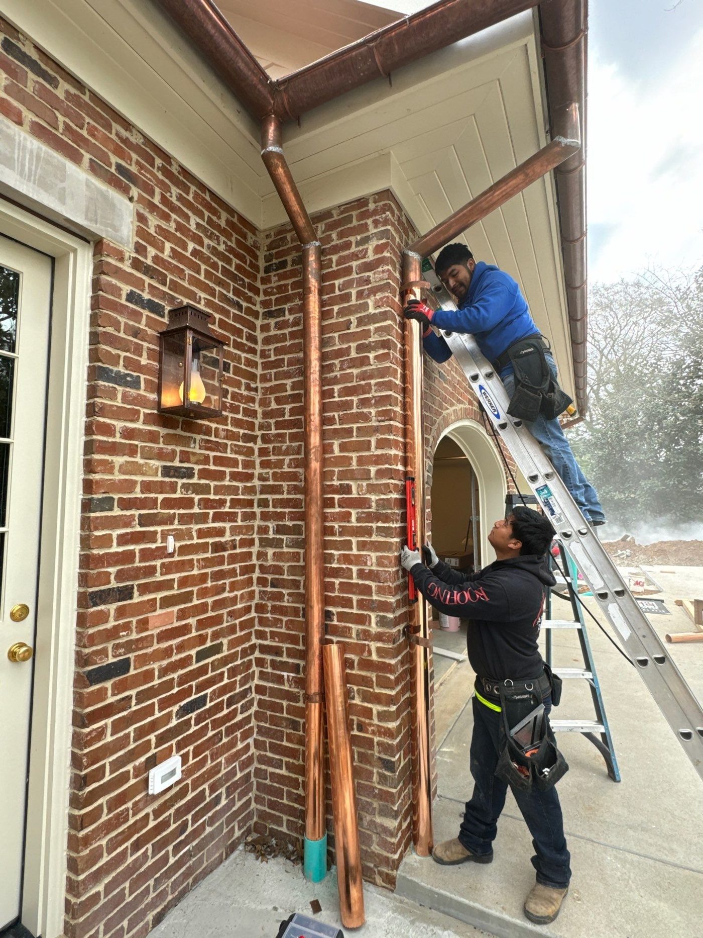 Crew installing copper gutters and downspouts on a brick chimney